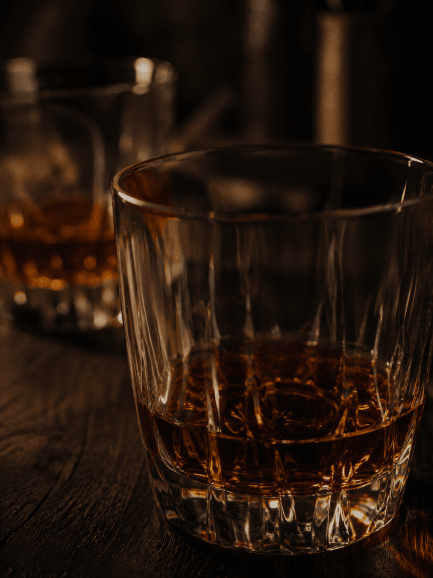A cut-crystal tumbler of bourbon on a dark bar top
